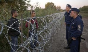 Syrian refugees and Hungarian police chat at the barbed wire fence at the border between Serbia and Hungary, in Roszke, Hungary Friday, Aug. 28, 2015. Hungary deployed police reinforcements to rein in an unrelenting flow of migrants across its porous border Thursday, but refugee activists said the effort appeared futile in a nation whose migrant camps are overloaded and barely delay their journeys west into the heart of the European Union. (ANSA/AP Photo/Darko Bandic)