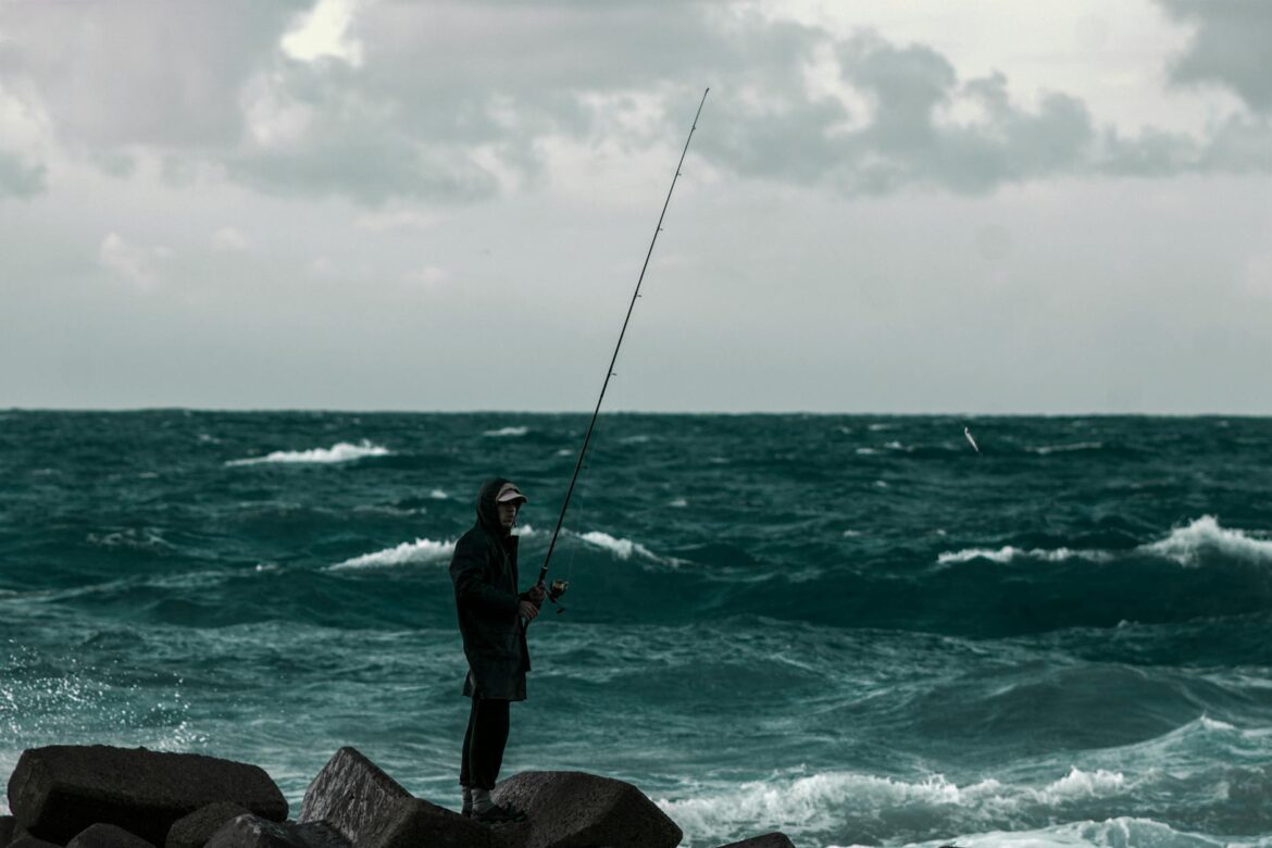 man fishing and standing on rocks beside the sea