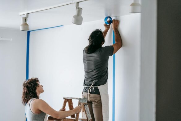 man putting tape on wall with woman holding the stepladder